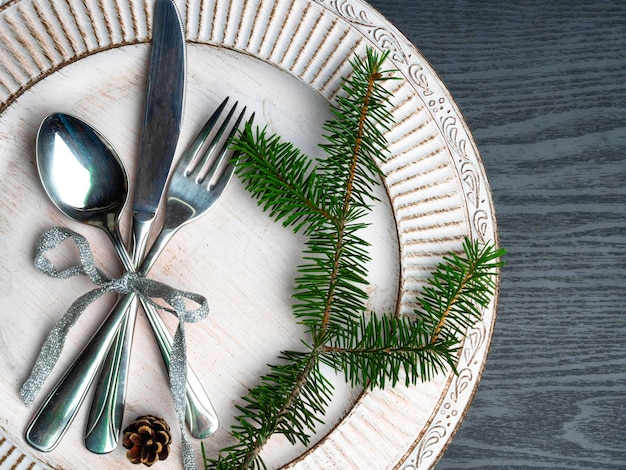 Cenário de mesa de natal vintage ou rústico Talheres de prato branco elegante e galho de pinheiro natural na superfície de madeira