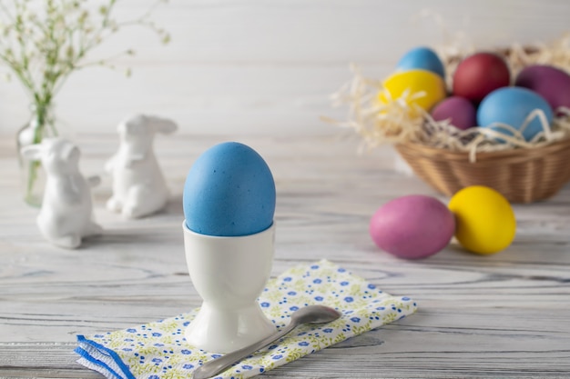 Foto cenário de mesa feliz páscoa com ovo azul tingido no copo, cesta com ovos coloridos e coelhos de cerâmica
