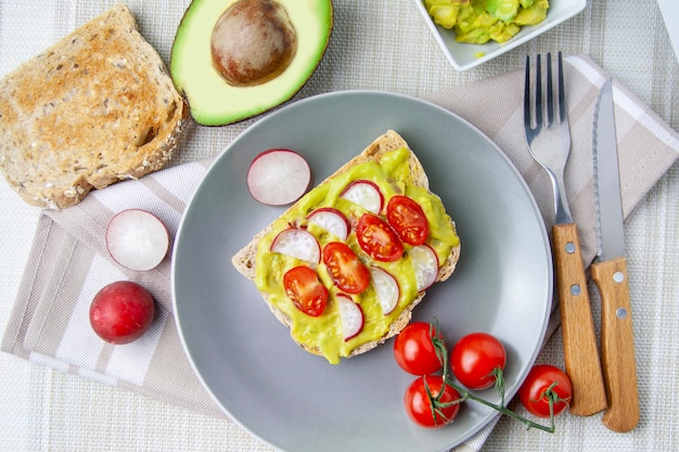 Cenital-Ansicht des Toasts mit Avocado, Tomate und Rettich auf einer grauen Platte