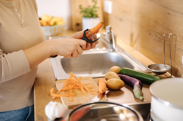 Cenoura de casca feminina usando descascador de legumes Fechamento da mão de uma mulher na cozinha Preparando comida em casa