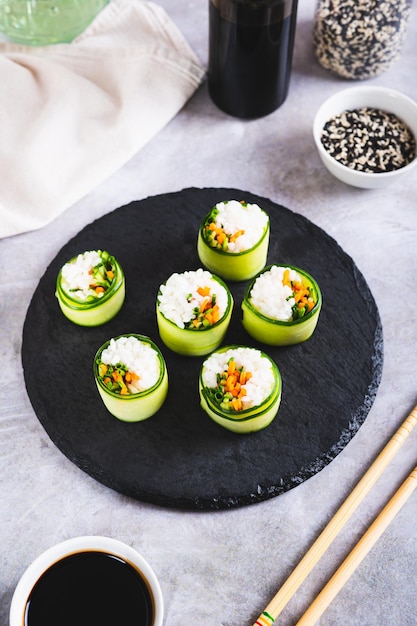 Foto cenouras de arroz de sushi vegetariano e cebolas verdes embrulhadas em pepino em uma placa de ardósia, vista vertical