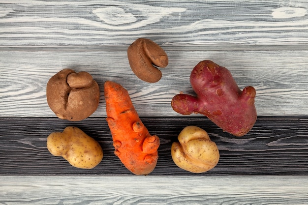 Cenouras e batatas defeituosas Forma anormal de vegetais deformados na vista superior de fundo de madeira