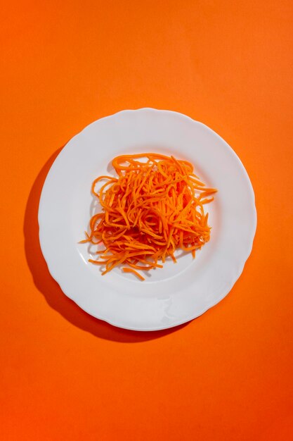 Cenouras em fatias finas em um prato branco em uma vista superior de fundo laranja