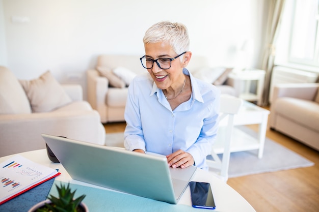 Centrado anciana con cabello blanco en casa usando laptop