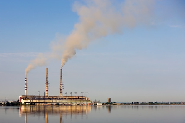 Central térmica de altas tuberías con espeso humo reflejado en la superficie del agua lke. Concepto de contaminación del medio ambiente.