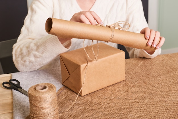 Centrarse en las manos de la mujer en caja de embalaje suéter de punto blanco. Papel de regalo artesanal y cordel natural. Felices vacaciones presente, sorpresa. Regalos para el dia de boxeo