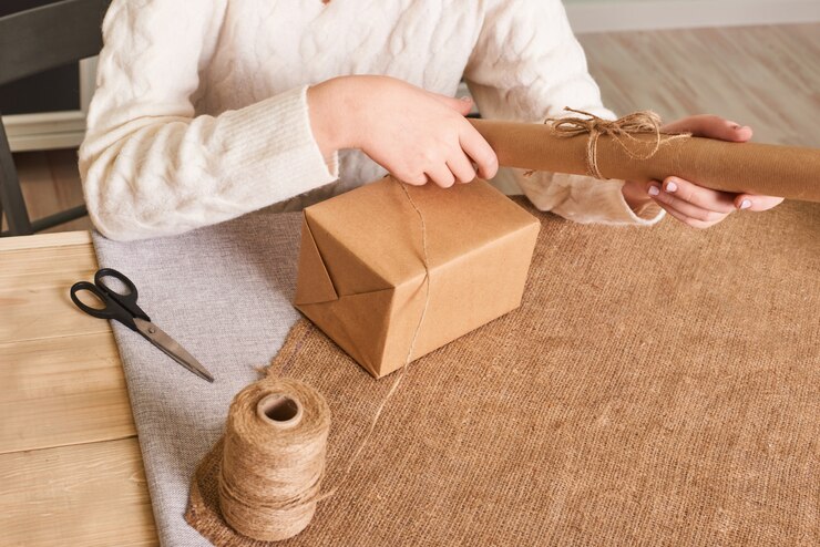 Foto centrarse en las manos de la mujer en caja de embalaje suéter de punto blanco. papel de regalo artesanal y cordel natural. felices vacaciones presente, sorpresa. regalos para el dia de boxeo
