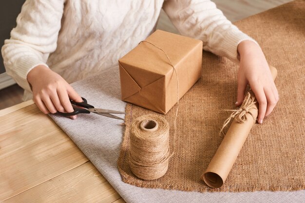 Centrarse en las manos de la mujer en caja de embalaje suéter de punto blanco. Papel de regalo artesanal y cordel natural. Felices vacaciones presente, sorpresa. Regalos para el dia de boxeo