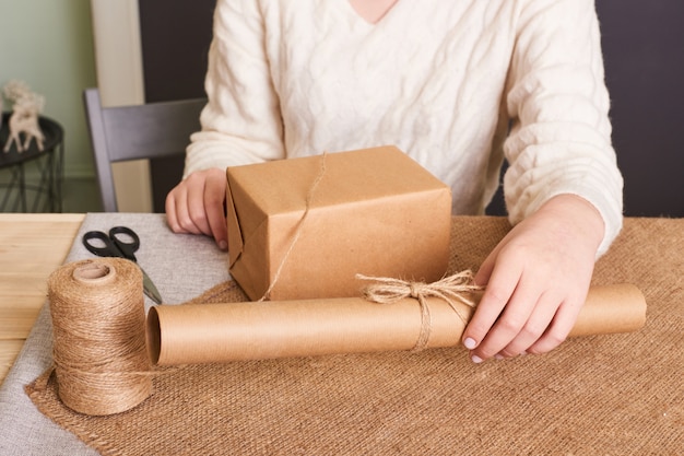 Centrarse en las manos de la mujer en caja de embalaje suéter de punto blanco. Papel de regalo artesanal y cordel natural. Felices vacaciones presente, sorpresa. Regalos para el dia de boxeo