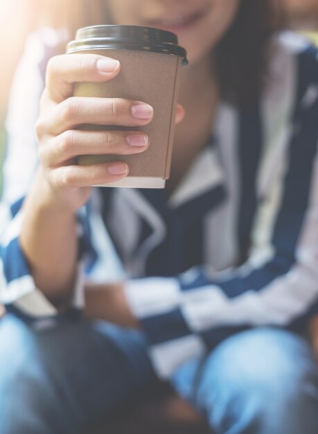 Centrarse en la taza de café. Mujer asiática relajada que sostiene una taza de café.