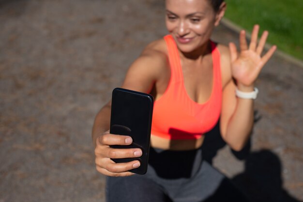 Centrarse en el teléfono inteligente negro en la mano de una mujer sonriente sentada en una forma de correr