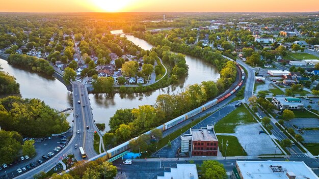 El centro de la ciudad y el tren con puente sobre la curva serpenteante del río a la aldea del vecindario paisaje urbano aéreo