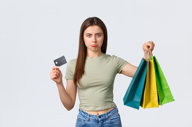 Centro comercial, estilo de vida e conceito de moda. Mulher fofa de beicinho decepcionada e chateada mostrando cartão de crédito vazio e sacolas com roupas, reclamando de não ter muito dinheiro