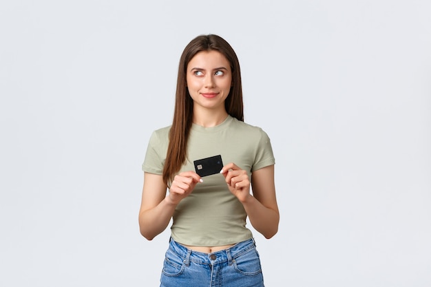 Centro comercial, estilo de vida y concepto de moda. Mujer contenta pensativa pensando qué comprar en todas las cuentas bancarias de dinero, mirando a la izquierda con una sonrisa complacida y sosteniendo la tarjeta de crédito.