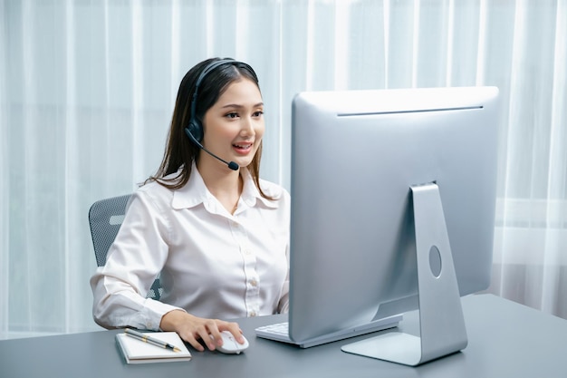 Centro de llamadas asiático entusiasta con auriculares y micrófono trabajando en su computadora portátil