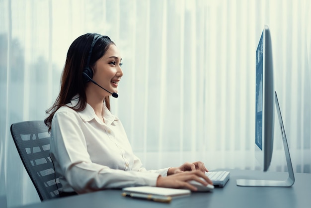 Centro de llamadas asiático entusiasta con auriculares y micrófono trabajando en su computadora portátil