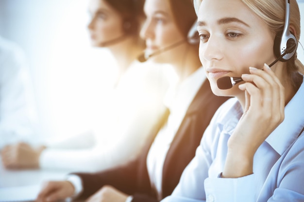 Centro de llamadas y concepto de gente de negocios. Hermosa mujer de negocios con auriculares consultando a clientes. Grupo de operadores telefónicos diversos en el trabajo en la oficina.