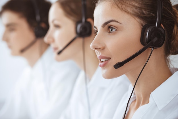 Centro de llamadas. Hermosa joven usando auriculares y computadora para ayudar a los clientes. Concepto de negocio