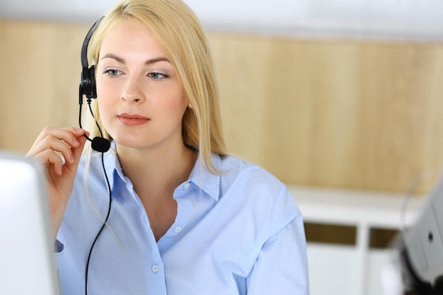 Centro de llamadas Mujer de negocios rubia sentada en auriculares en la oficina de servicio al cliente