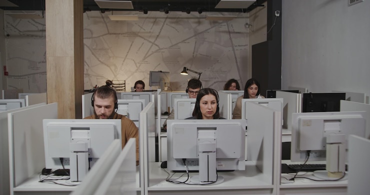 Foto centro de llamadas con trabajadores en micrófonos con auriculares hablando con clientes