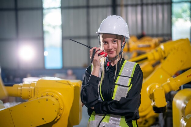El centro de robótica industrial muestra a una ingeniera supervisando las operaciones con un dispositivo de comunicación en medio de brazos robóticos amarillos