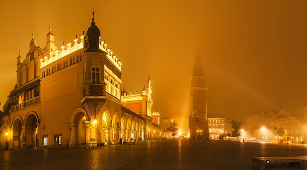 Los centros comerciales Sukiennice y el resto de la torre del ayuntamiento en la plaza principal de Cracovia en la noche brumosa con cielo dorado