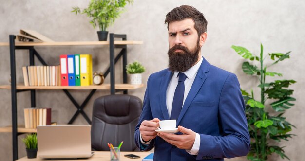 Ceo brutal em traje de negócios tem almoço com xícara de café no escritório