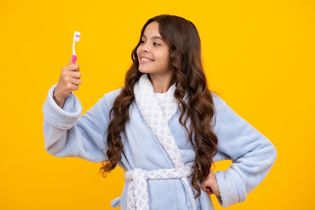 Cepillarse los dientes de noche Chica limpia sus dientes con un cepillo Retrato hermosa adolescente sosteniendo cepillo de dientes cepillarse los dientes aislado sobre fondo amarillo Concepto de salud dental
