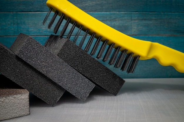 Cepillo de alambre de plástico amarillo con esponjas de lijado rectangulares apiladas inclinadas contra la pared de madera azul