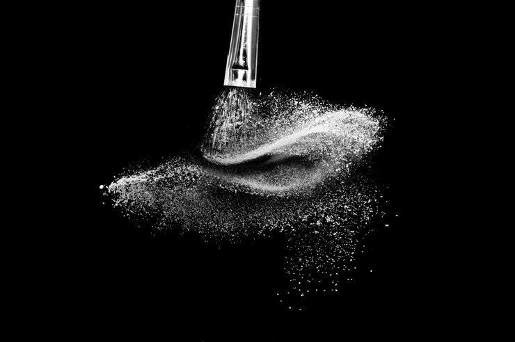 Foto cepillo cosmético con polvos cosméticos blancos que se extienden para maquillador o diseño gráfico en fondo negro