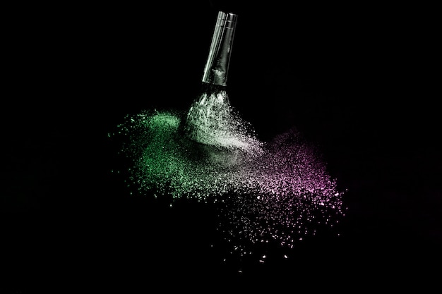 Cepillo cosmético con polvos cosméticos verdes y rosados que se extienden para maquillador y diseño gráfico en fondo negro