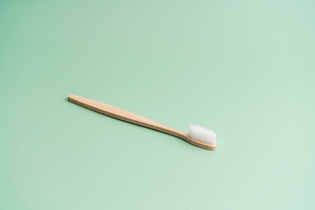 Cepillo de dientes antibacteriano de madera de bambú ecológico sobre fondo verde claro.