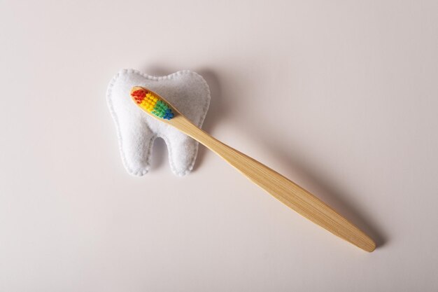 Un cepillo de dientes de bambú con cerdas multicolores yace sobre una figura de dientes de fieltro
