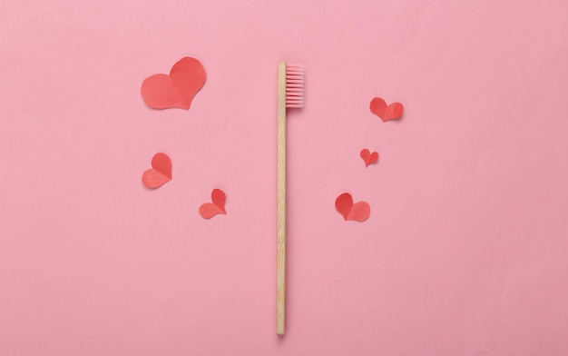 Cepillo de dientes de bambú ecológico y corazones sobre fondo rosa Concepto de amor romántico
