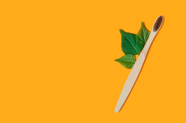 Foto cepillo de dientes de bambú con hojas verdes sobre naranja