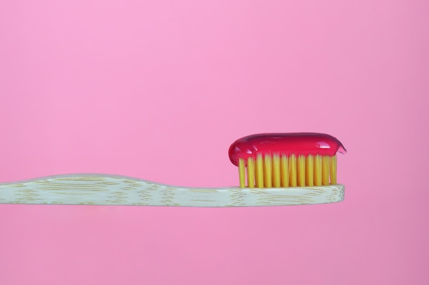 Cepillo de dientes de bambú con pasta resaltada en un fondo rosa Cuidado dental