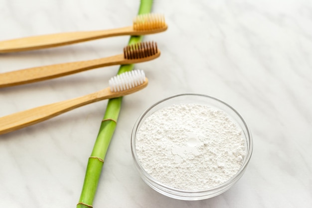 Cepillo de dientes de bambú, polvo de dientes de dentífrico de plantas de bambú sobre fondo de mármol blanco.