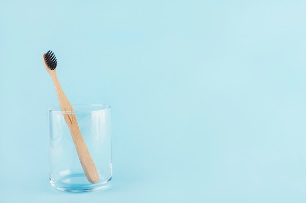 Cepillo de dientes de bambú y un vaso de agua.