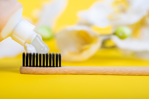 Cepillo de dientes ecológico de madera con pasta sobre un fondo amarillo con flores.