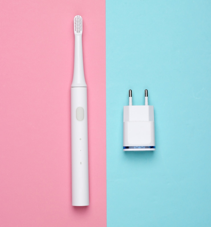Foto cepillo de dientes eléctrico moderno con cargador sobre un fondo rosa pastel azul. vista superior