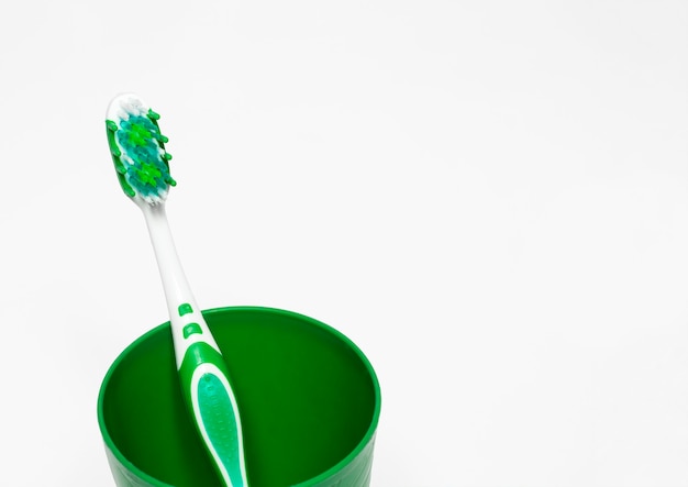 Un cepillo de dientes es verde en un vaso sobre un blanco con espacio para texto, cepillarse los dientes y cuidar la boca.