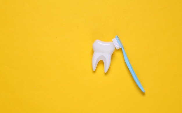 El cepillo de dientes limpia el diente de plástico falso sobre un fondo amarillo. Concepto de cuidado dental