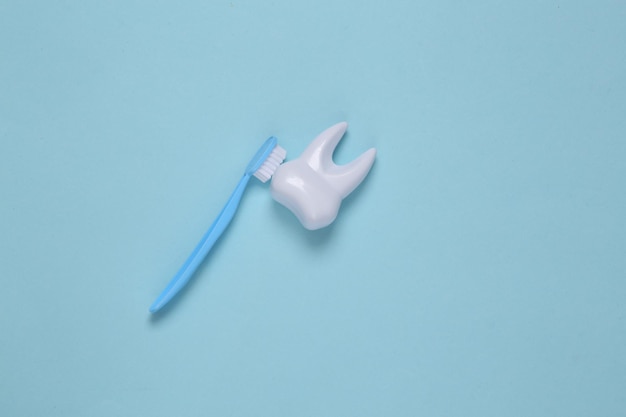El cepillo de dientes limpia el diente de plástico de juguete sobre fondo azul. Concepto de atención dental