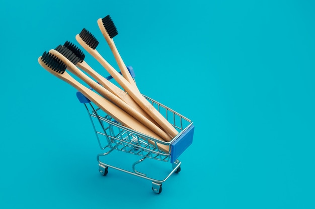 Cepillo de dientes de madera en carrito de compras sobre fondo azul.