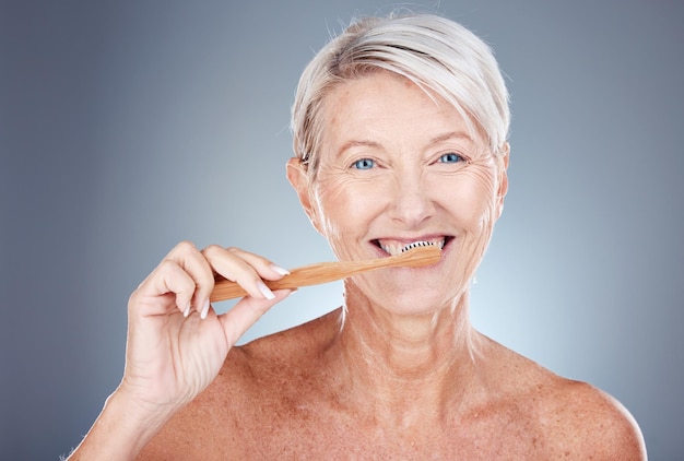 Cepillo de dientes de mujer madura y retrato para el bienestar de la salud y el cuidado bucal en un fondo de estudio gris Cepillarse los dientes limpios y una mujer mayor limpiando su boca para el cuidado bucal o la higiene dental