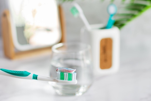 Cepillo de dientes con pasta de dientes en la mesa del baño con un vaso de agua Concepto de higiene dental