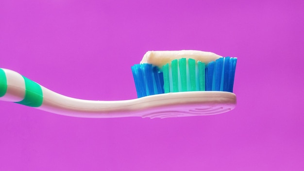 Cepillo de dientes con pasta de dientes sobre un fondo morado, cuidado dental