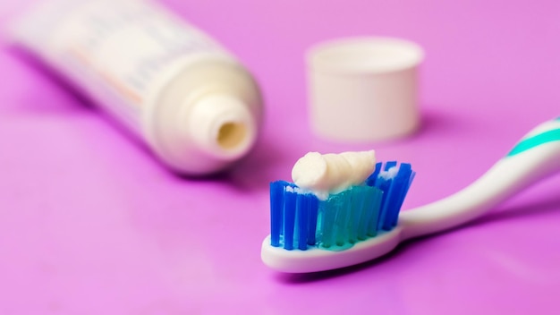 Cepillo de dientes y tubo de pasta de dientes sobre un fondo morado. Cuidado dental