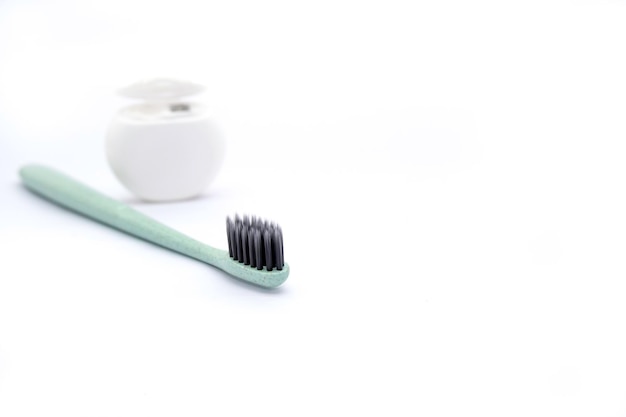 Cepillo de dientes verde con cerdas finas negras y hilo dental blanco sobre fondo blanco con espacio para copiar