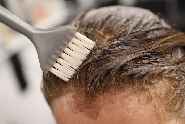 Cepillo gris aplicar tinte para el cabello a la cabeza de cerca.